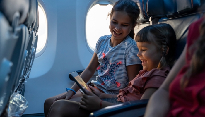 Cute Kids sit at the window of an airplane and use a digital tablet during the flight.