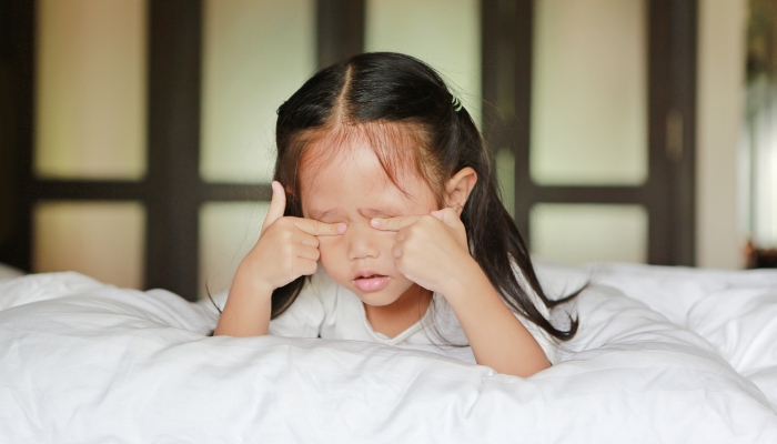 Cute little asian girl in lying on a bed squeezing eyes.