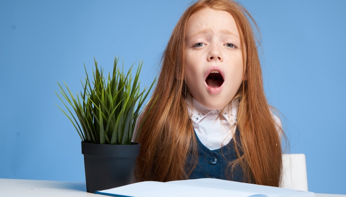 Emotional red-haired girl sitting at the table home lessons learning.