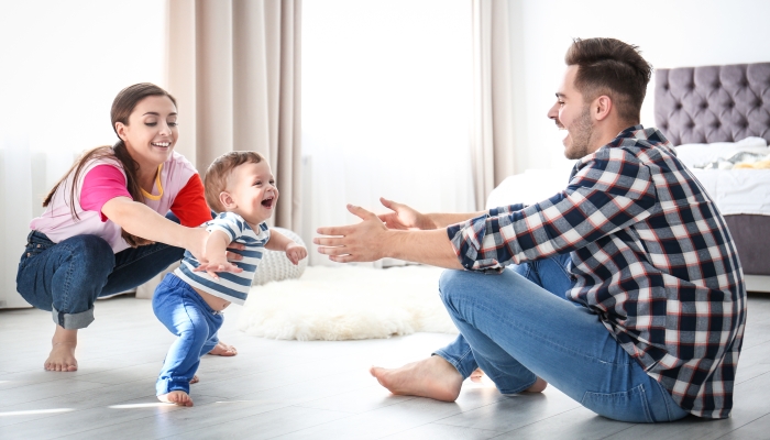 Happy family playing and baby learning to walk at home.