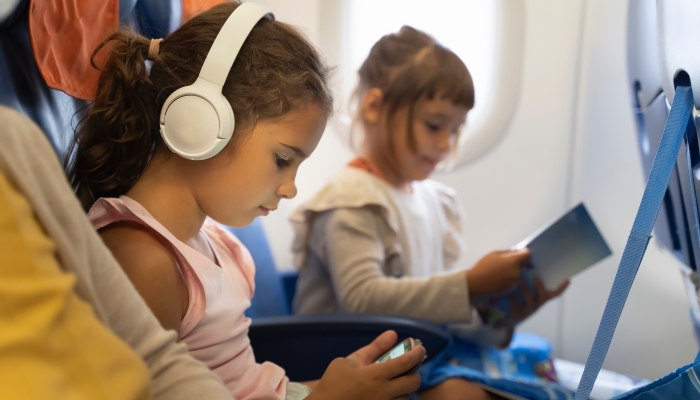 Kid schoolgirl in headphones watches cartoons in a phone on an airplane.