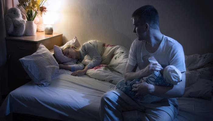 Married young adult feeding their child in a bottle at night.