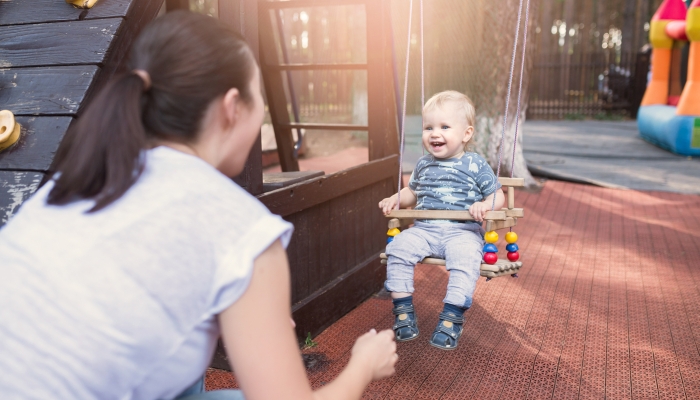 Mom swinging baby boy in swing at summer time.