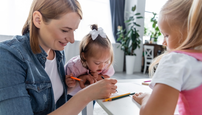 Mom writing near toddler kid with down syndrome and preschooler girl.