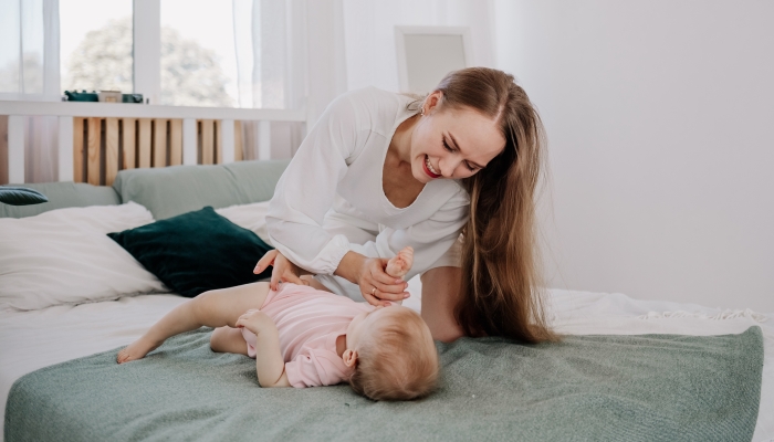 Mother teaches her baby to roll over on her stomach on the bed.