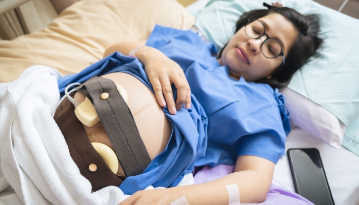 The expectant mother is lying in the hospital bed and is wearing a Fetal Doptone to prepare for the caesarean section.