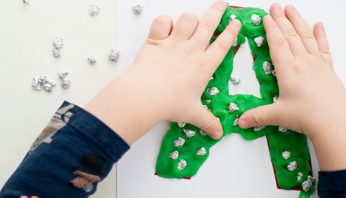 Two year boy decorating play dough letter A with aluminum foil balls.