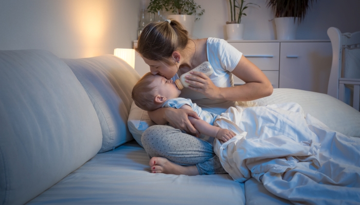 Young mother feeding her baby from bottle in bed at night.