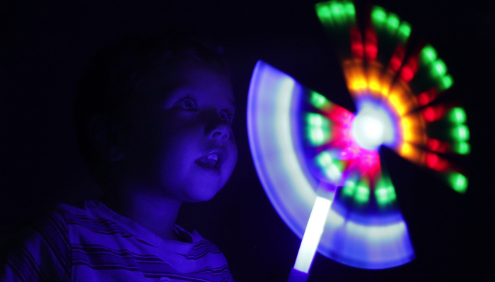 Young boy looking at a light up toy in a dark room.