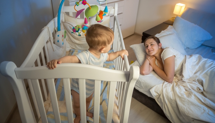 9 months old baby standing in crib and waking up his tired mother.