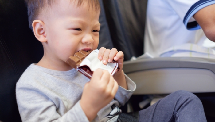 Asian baby boy eating chocolate bar during flight on airplane.