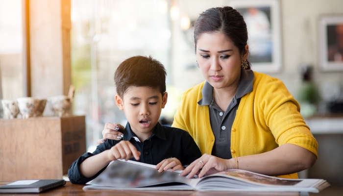 Asian mother teaching her son read a book.