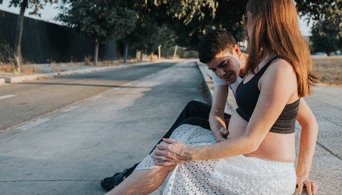 Attractive young caucasian pregnant couple sitting on the curb.