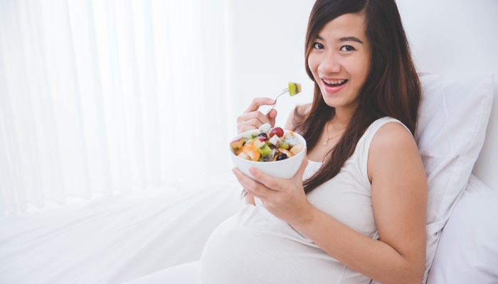 Beautiful pregnant woman with a bowl of fruit.