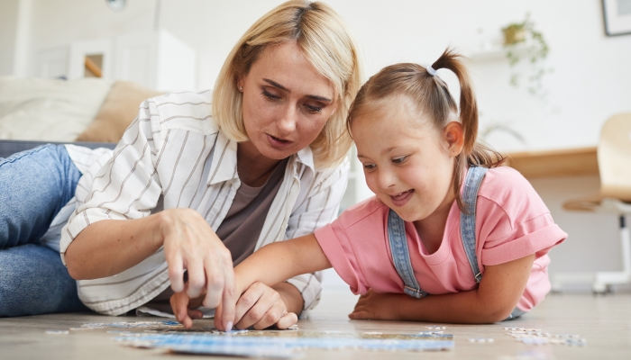 Mother teaching her daughter with down syndrome collecting puzzles.