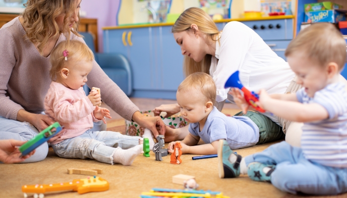 Friends with children toddlers playing on the floor in montessori centre.