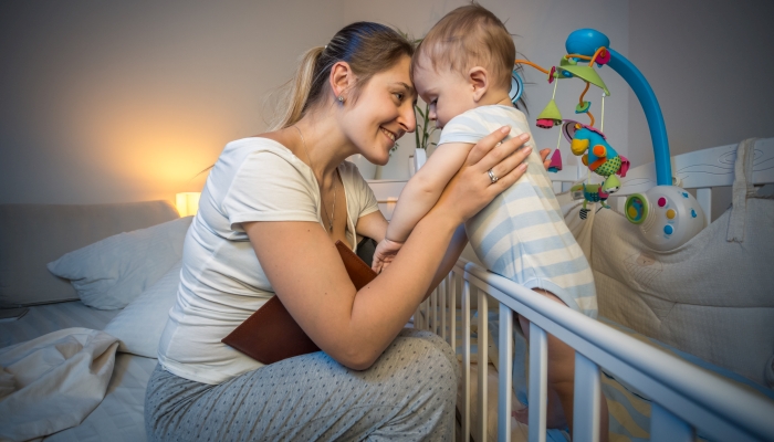 Happy young mother looking at her baby in crib before going to sleep.