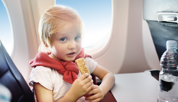 Little boy drinking water and eating snack during the flight.