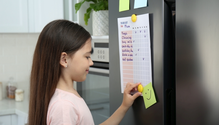 Little girl putting to do list on fridge in kitchen.