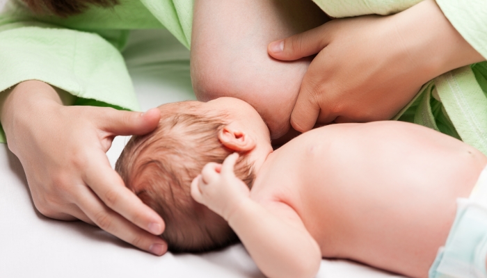 Little newborn baby child sucking or eating mother breast milk.