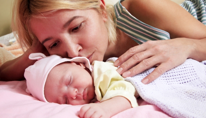 Mother with her sleeping newborn baby in home.