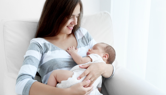 Portrait of pretty young woman holding sleeping baby at home.