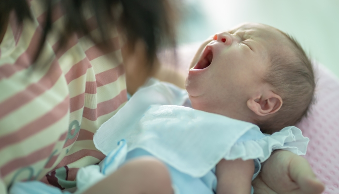 Six month old baby was yawning on her mother's arms.