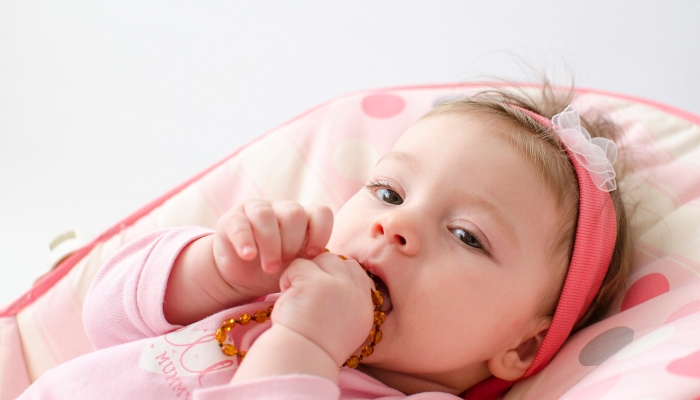 Teething baby girl using a teething necklace.