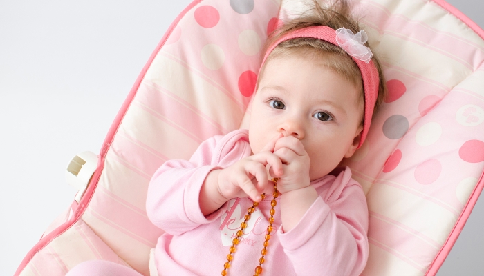 Beautiful baby girl chewing amber teething necklace.