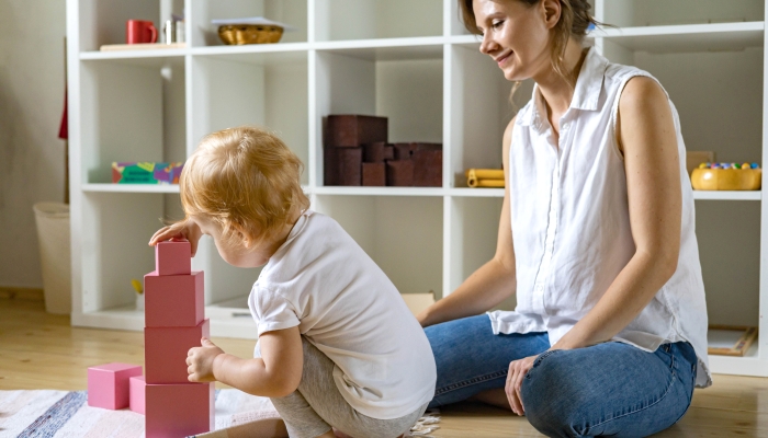 Young mother and little baby assembling pink cube Maria Montessori ecological materials.