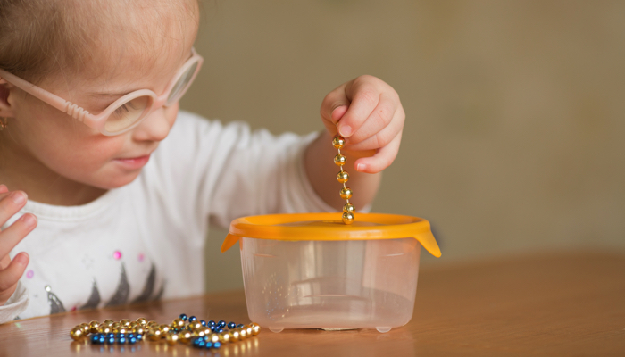 Little girl pulling beads out of a container.