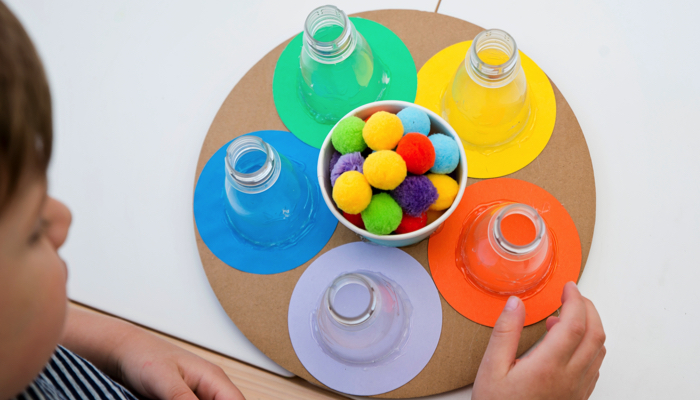 A little boy playing with pom poms and bottles in a fine motor game.
