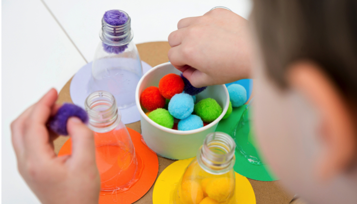 A little boy playing with pom poms and bottles in a fine motor game.