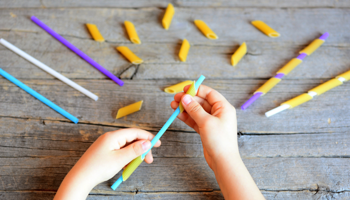 A little girl stringing pasta on straws.