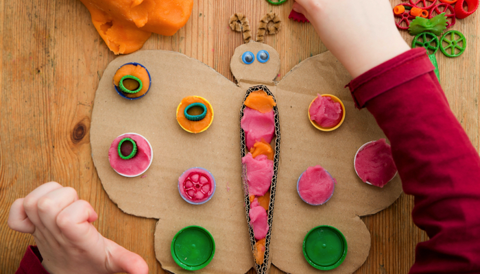 Little girl decorating a cardboard butterfly with play dough and dried pasta.