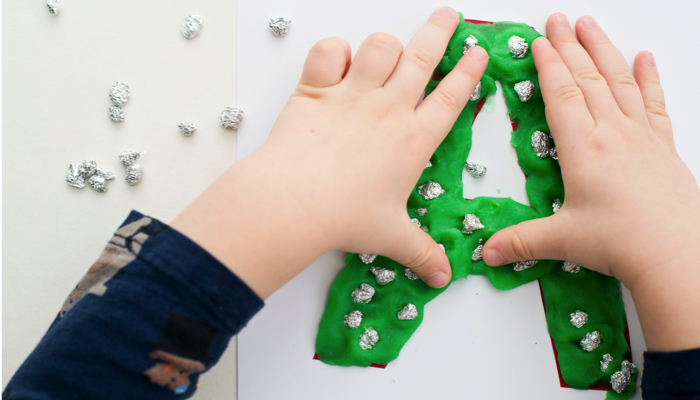 Little boy making a letter A out of play dough.