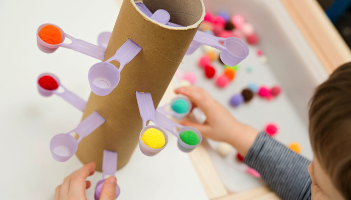 Little boy placing pom pots in measuring spoons on a tower.