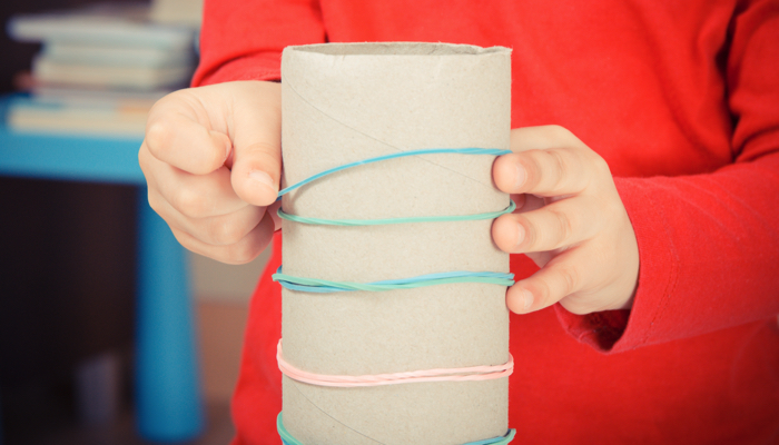 A little boy putting rubber bands on a cardboard tube.