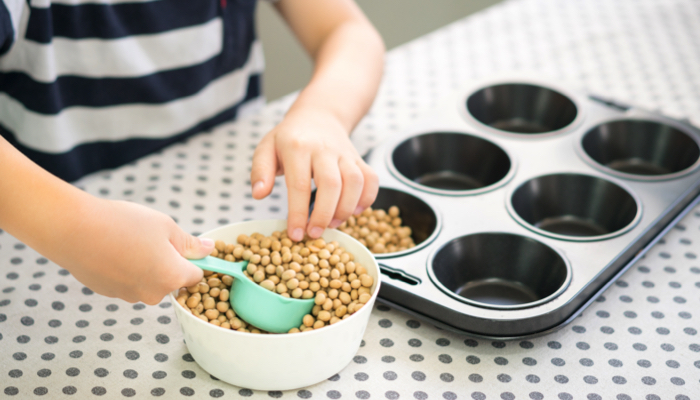 Little boy scooping beans form a bowl into a cupcake pan.