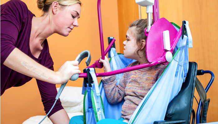 Caregiver using a lift to place a child in a wheelchair.