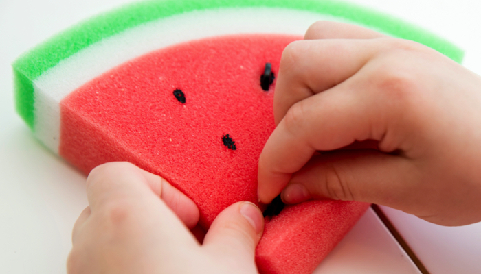 Child placing buttons in a watermelon shaped sponge.