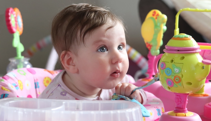 6 month old baby in exersaucer with beautiful blue eyes and brown hair.