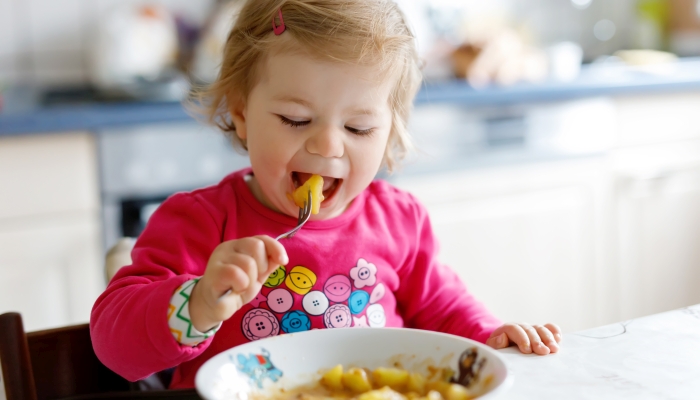 Adorable baby girl eating from fork vegetables and pasta.