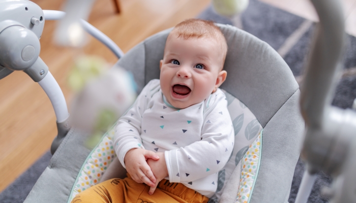 Adorable caucasian 6 months old baby boy sitting in his rocker chair, talking baby language and looking at toys.