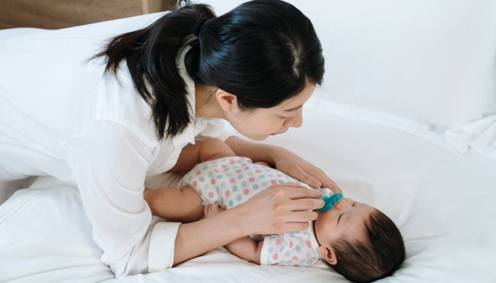 Asian millennial mom gently taking teether away from her young kid.