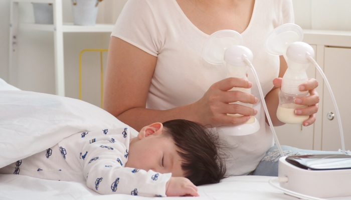Asian mother holding twin breast pump after feeding her child in the bedroom at home.