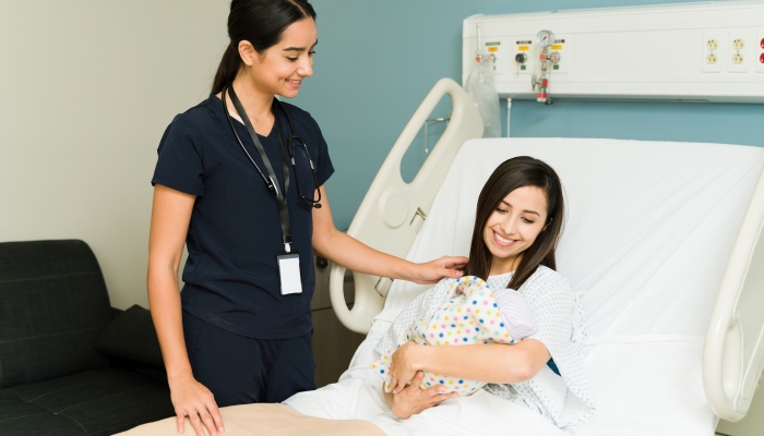 Attractive female nurse checking on the health of a woman and her newborn baby at the hospital.