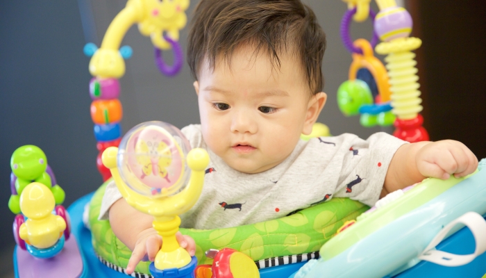 Baby boy playing toy in a exersaucer.