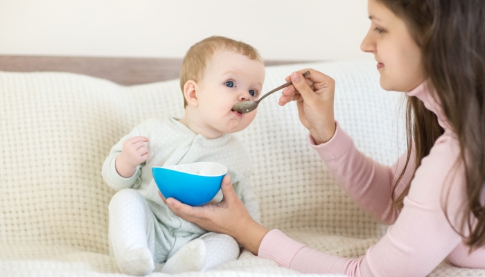 Baby eating while sitting on the bed.