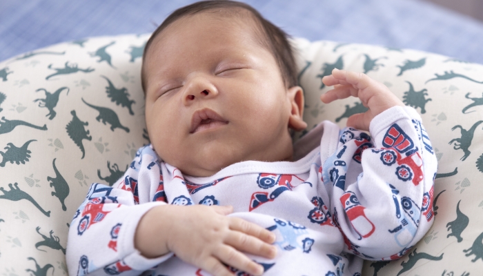 Baby very relaxed, in bed with dinosaur boppy pillow.